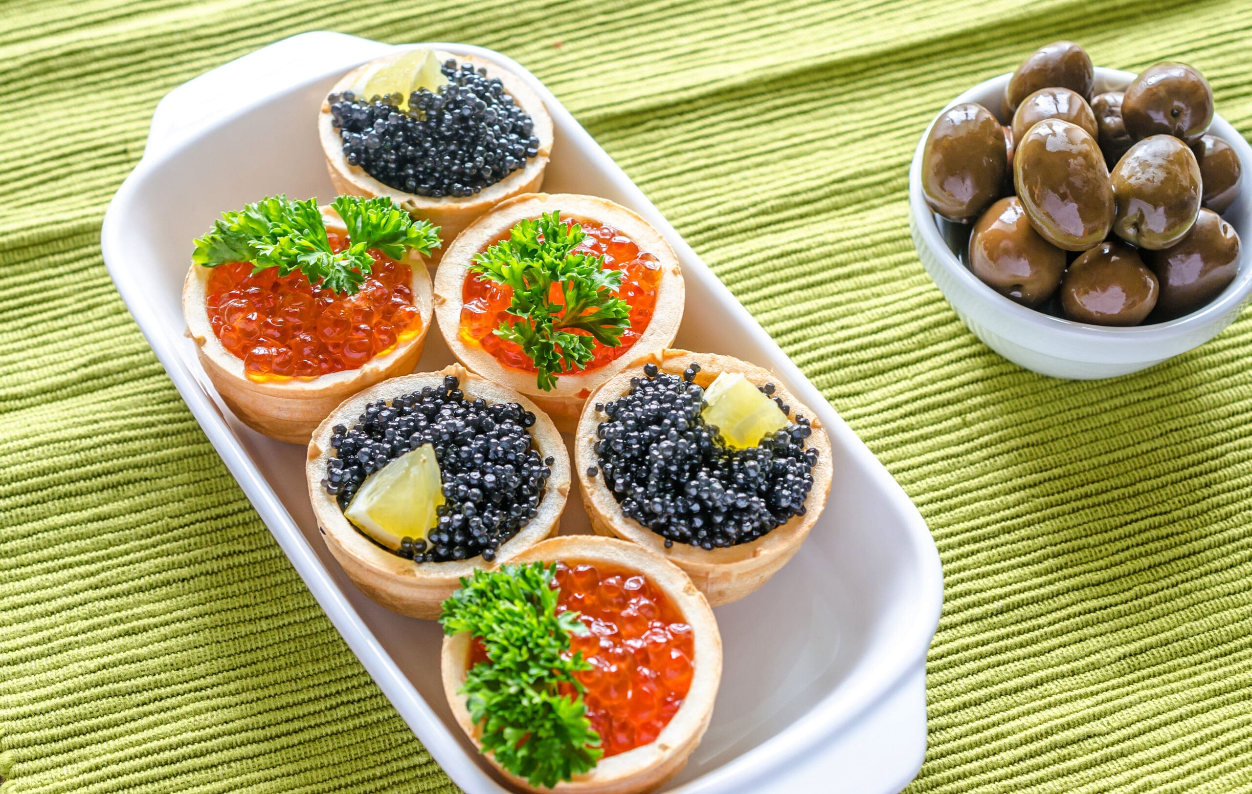 bowl of olives next to tartlets with Salmon roe and black caviar