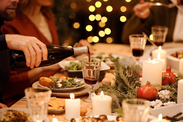 person pouring red wine into glass at upscale dinner party