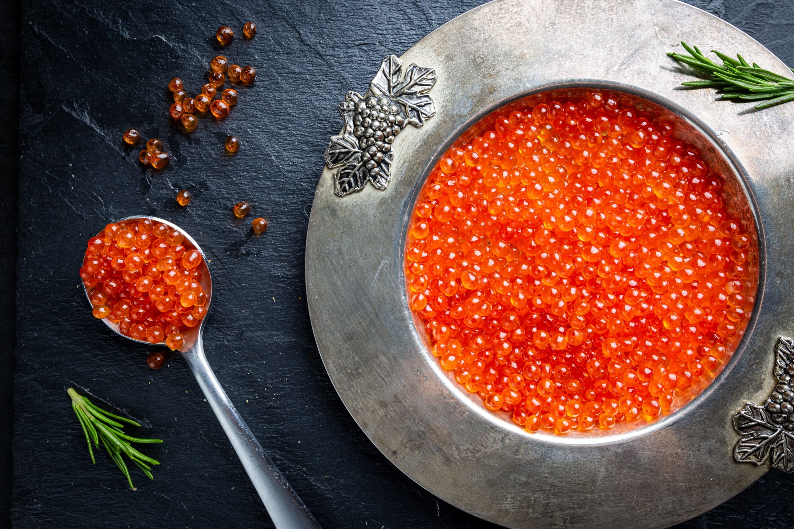 Red caviar in a bowl alongside spoonful of caviar