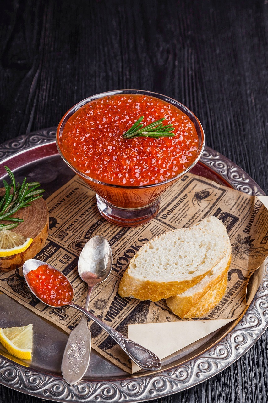 red roe in glass dish next to bread and spoons