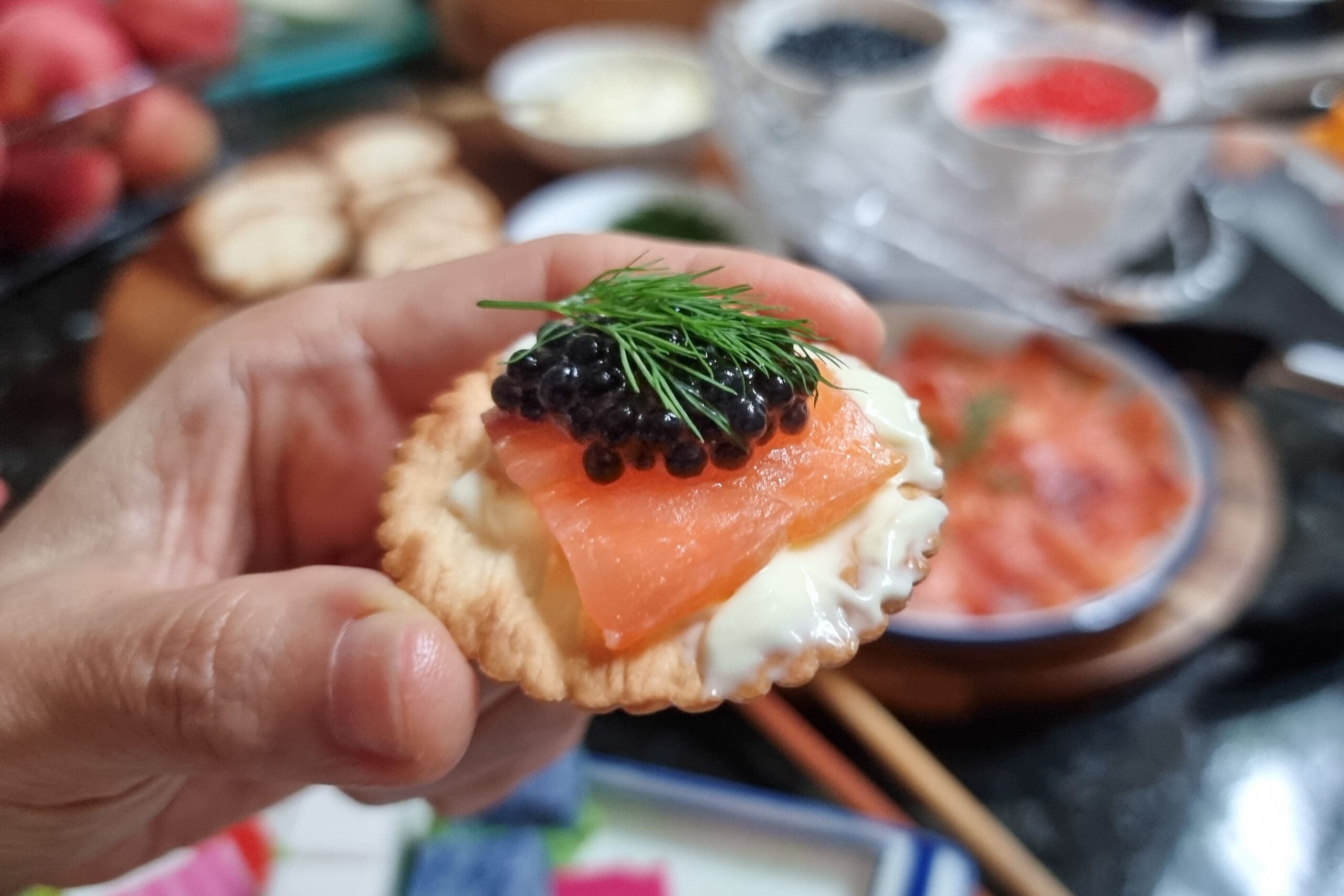 person holding cracker topped with smoked salmon and caviar