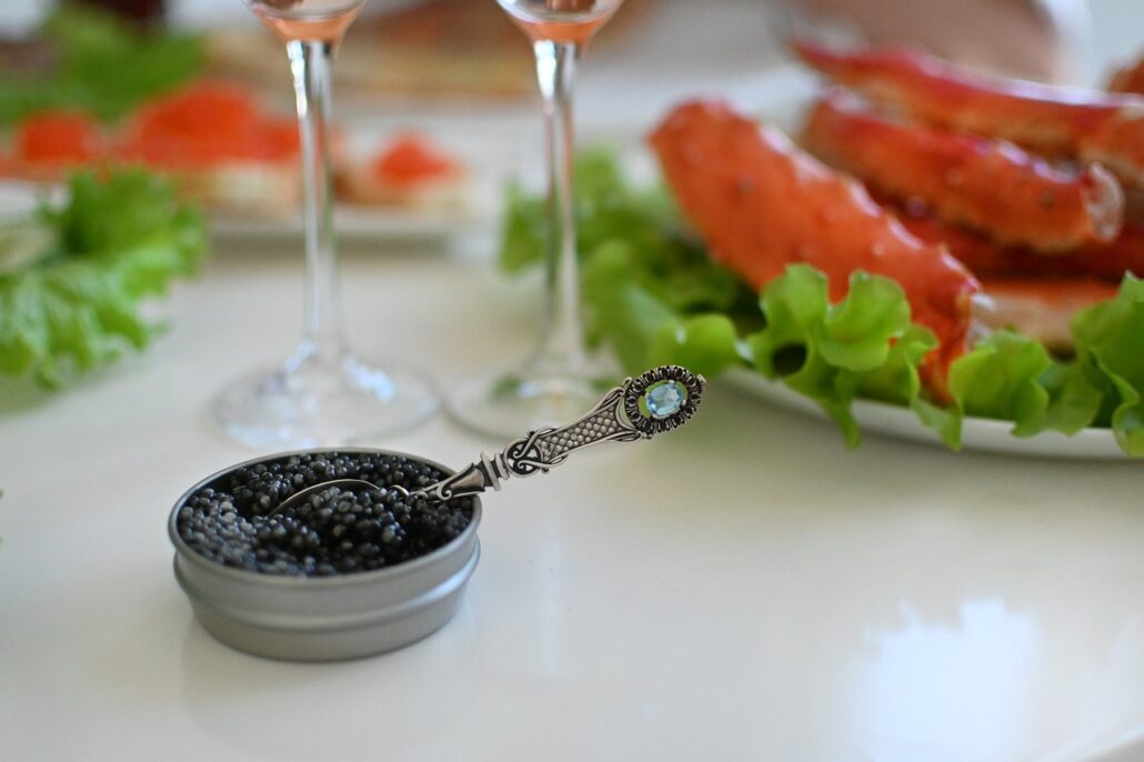 caviar in tin with spoon alongside plate of crab legs