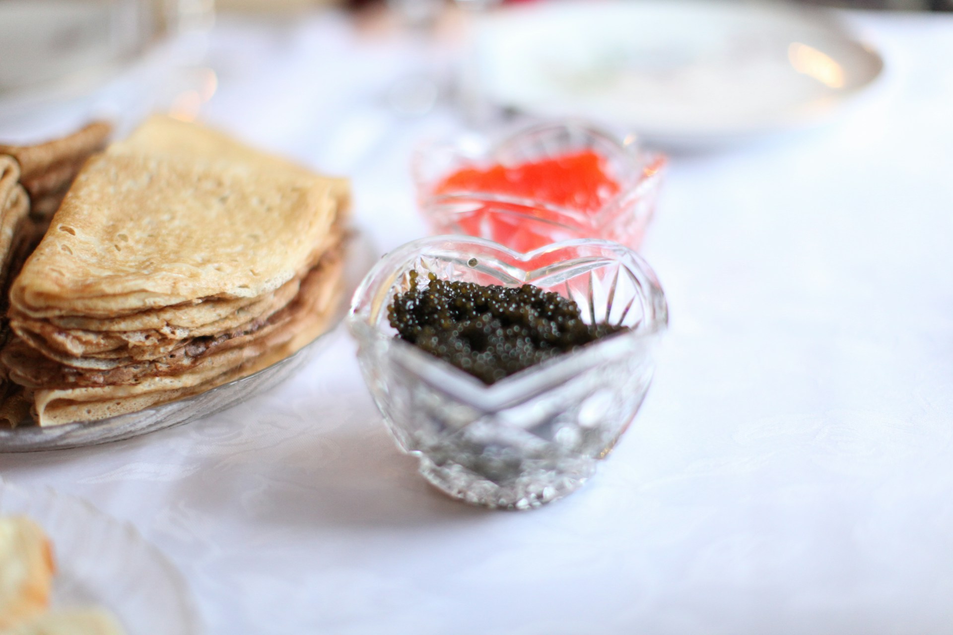 plate of pancakes and glass bowl of black caviar on table