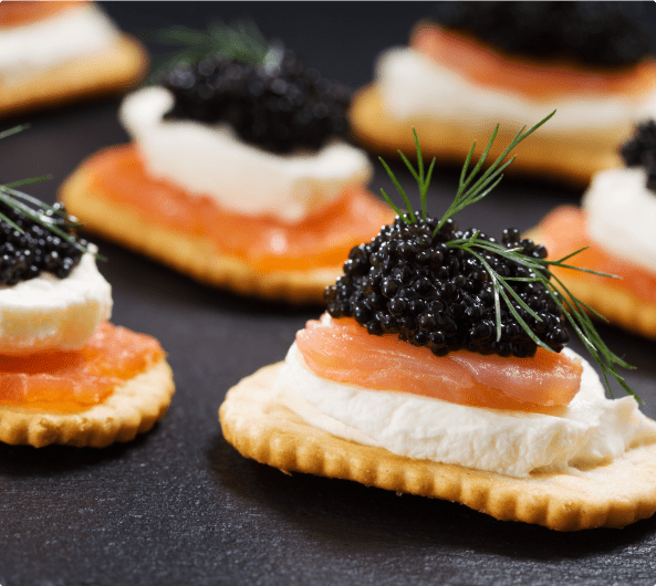 Black caviar appetizers with dill on top of smoked salmon, cream, and a cracker