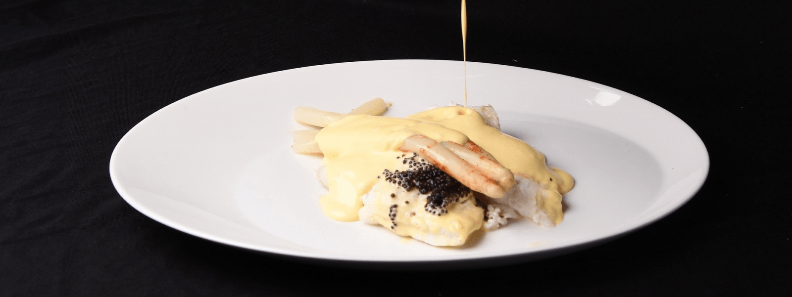 sauce pouring on plate of cod and caviar
